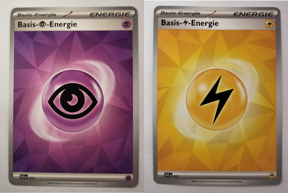 Zwei Basis-Energiekarten nebeneinander: Links die Psycho-Energie mit lila Hintergrund und einem schwarzen Auge-Symbol. Rechts die Elektro-Energie mit gelbem Hintergrund und einem schwarzen Blitz-Symbol. Beide Karten haben ein schlichtes, geometrisches Design.
