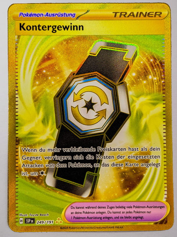 Goldene Trainerkarte ‚Kontergewinn‘ aus dem Pokémon-Sammelkartenspiel. Die Karte zeigt ein schwarzes Armband mit einem gold-blauen Symbol vor einem leuchtenden, goldenen Hintergrund. Sie reduziert die Energiekosten der Attacken eines Pokémon, wenn der Spieler mehr verbleibende Preiskarten hat als der Gegner.