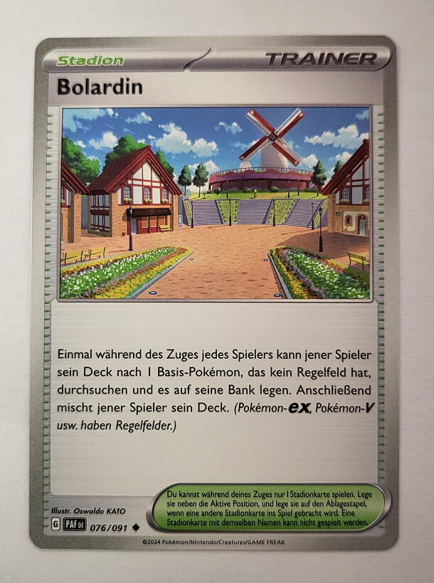 Pokémon-Stadionkarte ‚Bolardin‘ mit einer idyllischen Illustration eines kleinen Dorfplatzes mit Windmühle. Die Karte ermöglicht es Spielern, ein Basis-Pokémon ohne Regelfeld aus ihrem Deck auf die Bank zu legen. Silbernes Design mit grünem Stadion-Label.